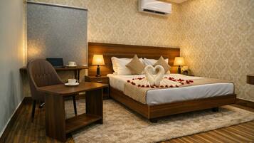 Une chambre d’hôtel avec un lit en bois, un bureau, une chaise, une télévision et un appareil de climatisation.