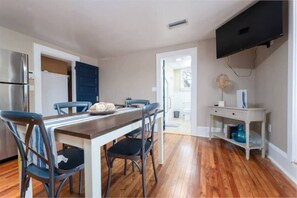 A modern kitchen with a dining area, wooden flooring, and a flat-screen TV mounted on the wall. - Charming 3-bedroom loft unit  with WiFi and AC in the Heart of San Marco (Jacksonville)
