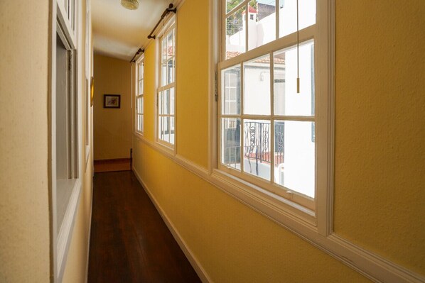 A narrow hallway with wooden flooring and large windows.