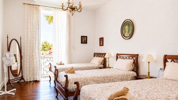 A hotel room with two beds, a sitting area with a chair and a table, a mirror, and a view of the outdoors. - Casa Los Profesores · Traditional Canarian Charm (La Orotava)