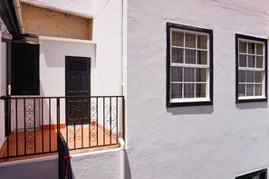 A white building with black shutters, a tiled patio, and a metal railing.