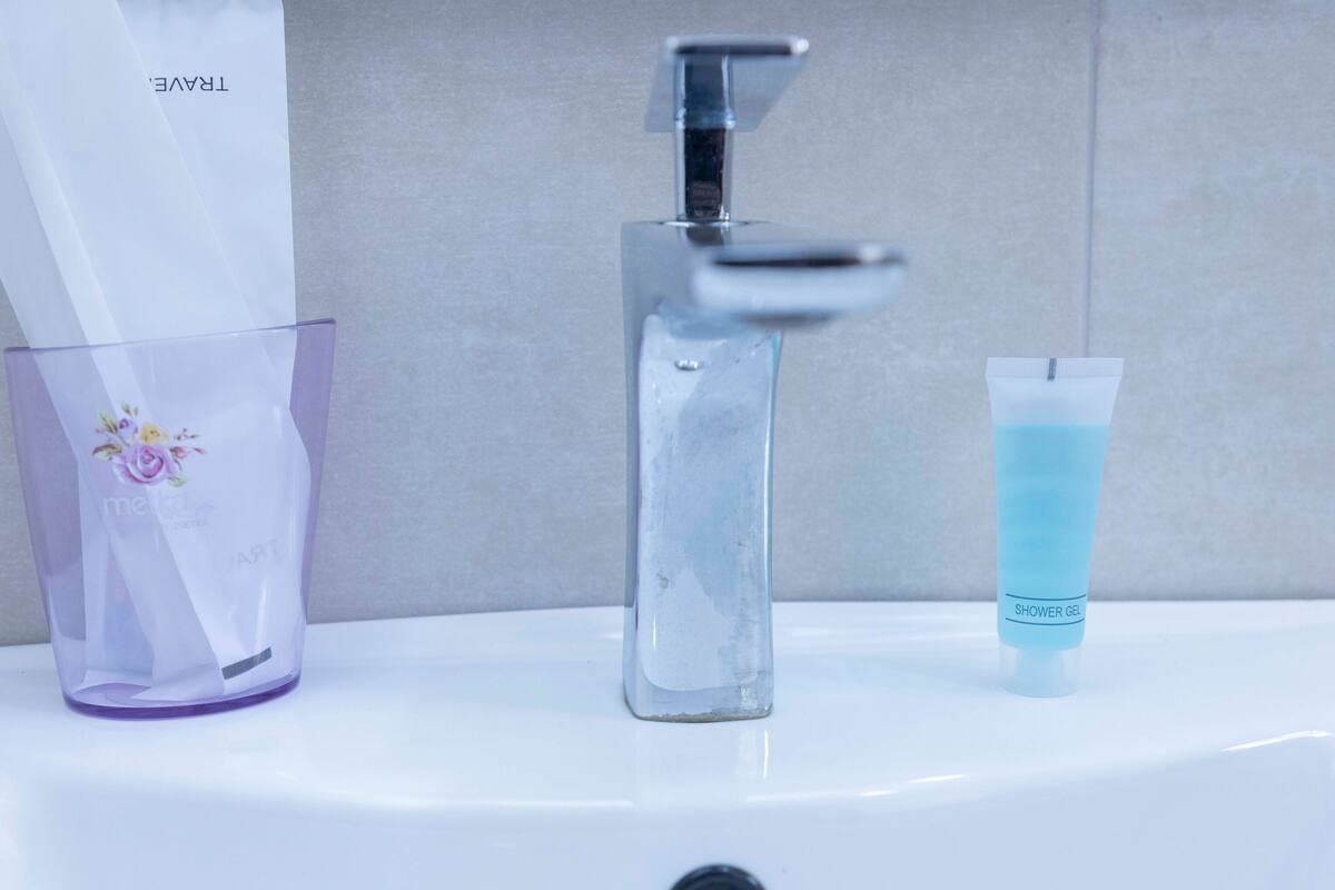 A bathroom sink with a modern faucet, a purple glass container with a floral design, and a tube of blue shower gel.
