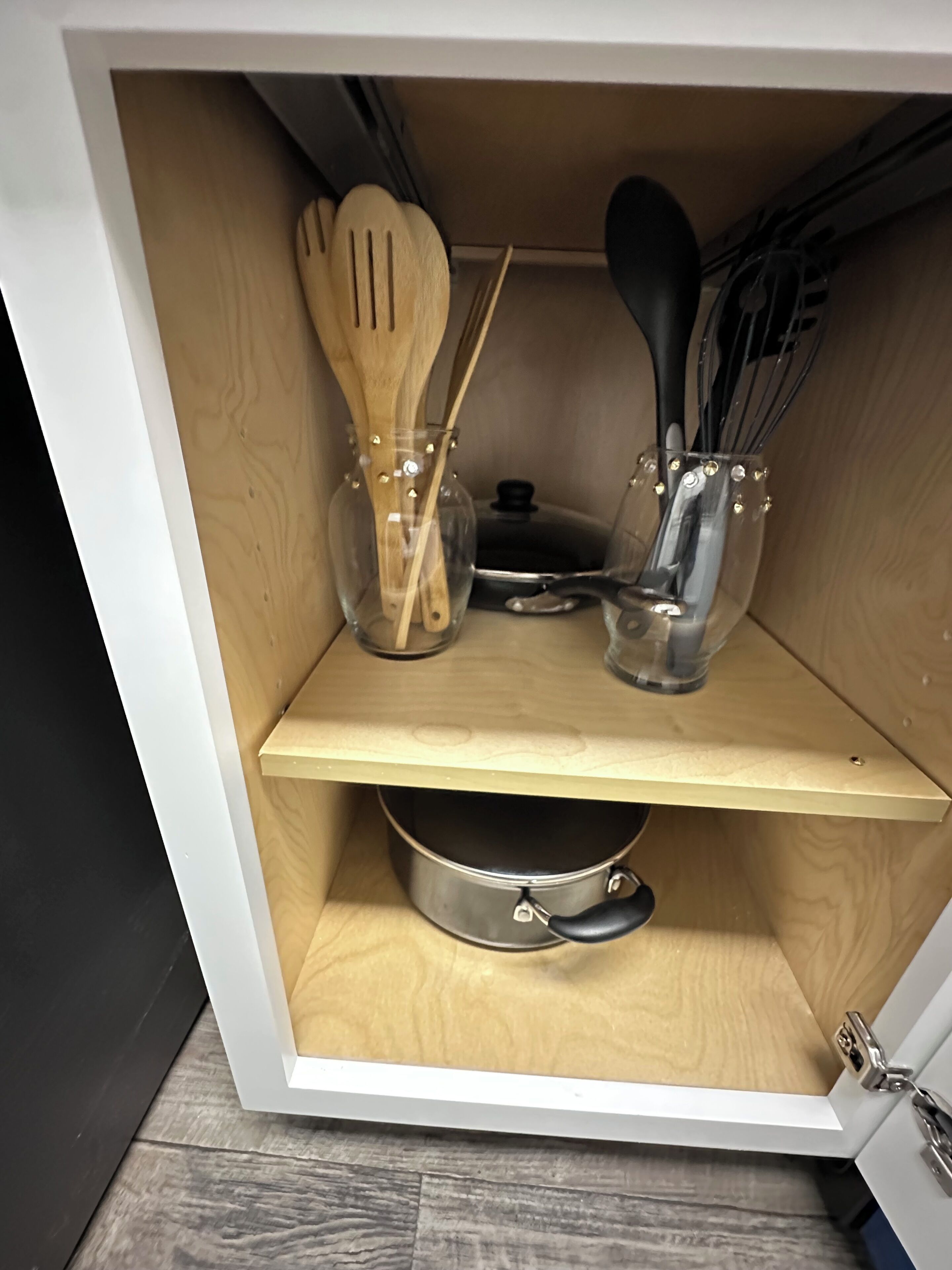 Ein Küchenschrank mit einer Holzwand, zwei Glasbehältern mit Metalldeckeln, einem Metalltopf und Küchenutensilien aus Holz und Metall.