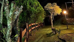 Um espaço ao ar livre à noite, com cerca de madeira, um poste de luz e uma montanha ao fundo.