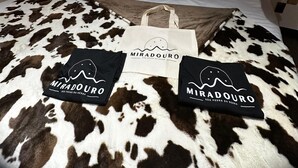 Uma cama com colcha estampada de vaca, duas almofadas com o mesmo padrão, uma cabeceira de madeira e um lustre suspenso.