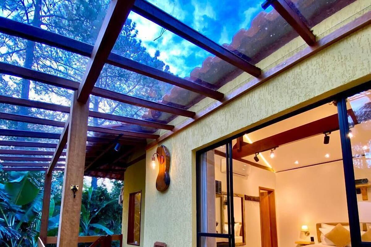 A wooden deck with a glass door leading to a bedroom with a bed and a nightstand.