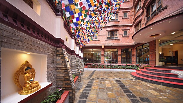 Un cortile con una statua di Buddha, pavimento in pietra e decorazioni pendenti colorate.