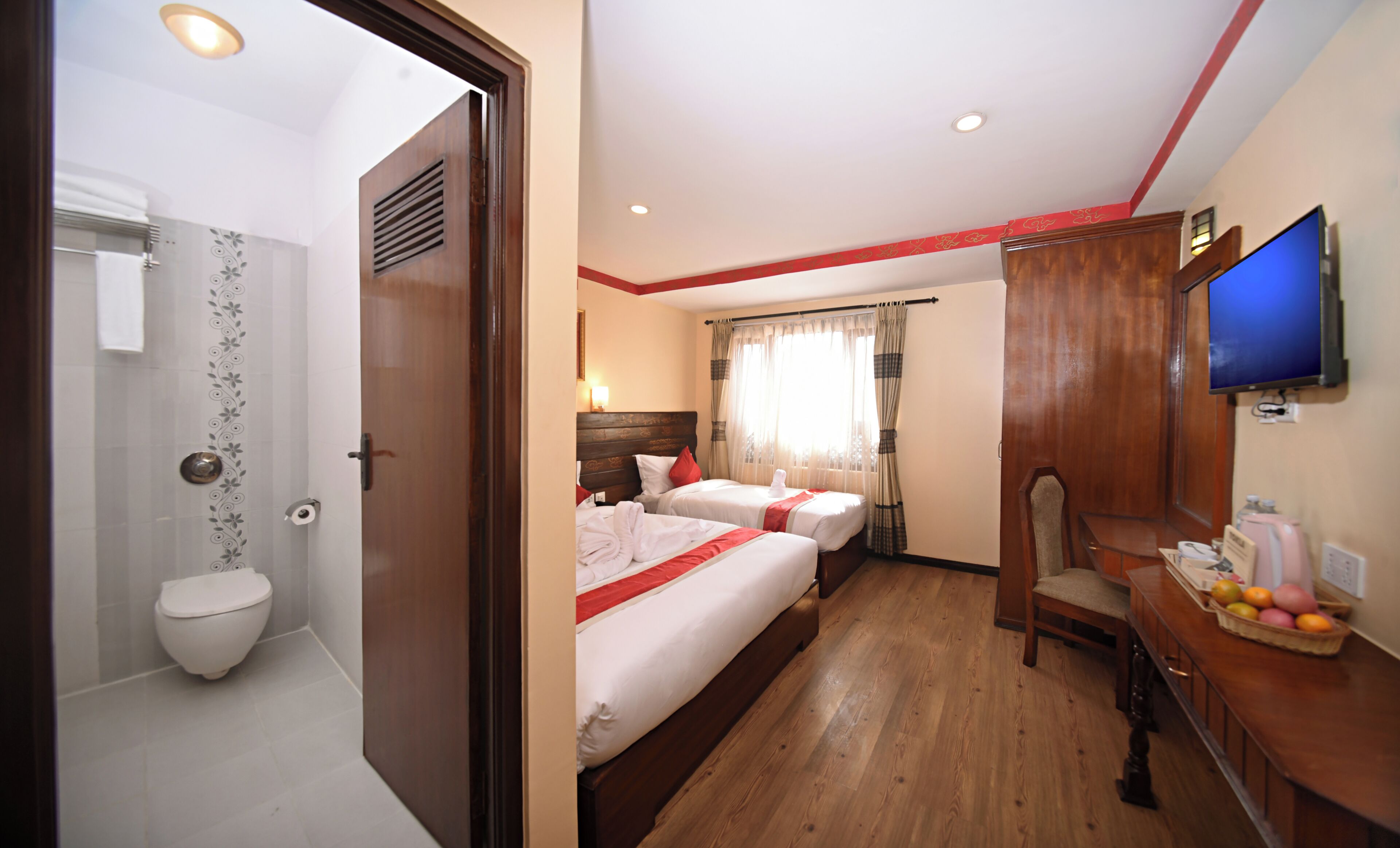 Habitación de hotel con dos camas, ducha, escritorio de madera, televisor y una cesta de frutas.