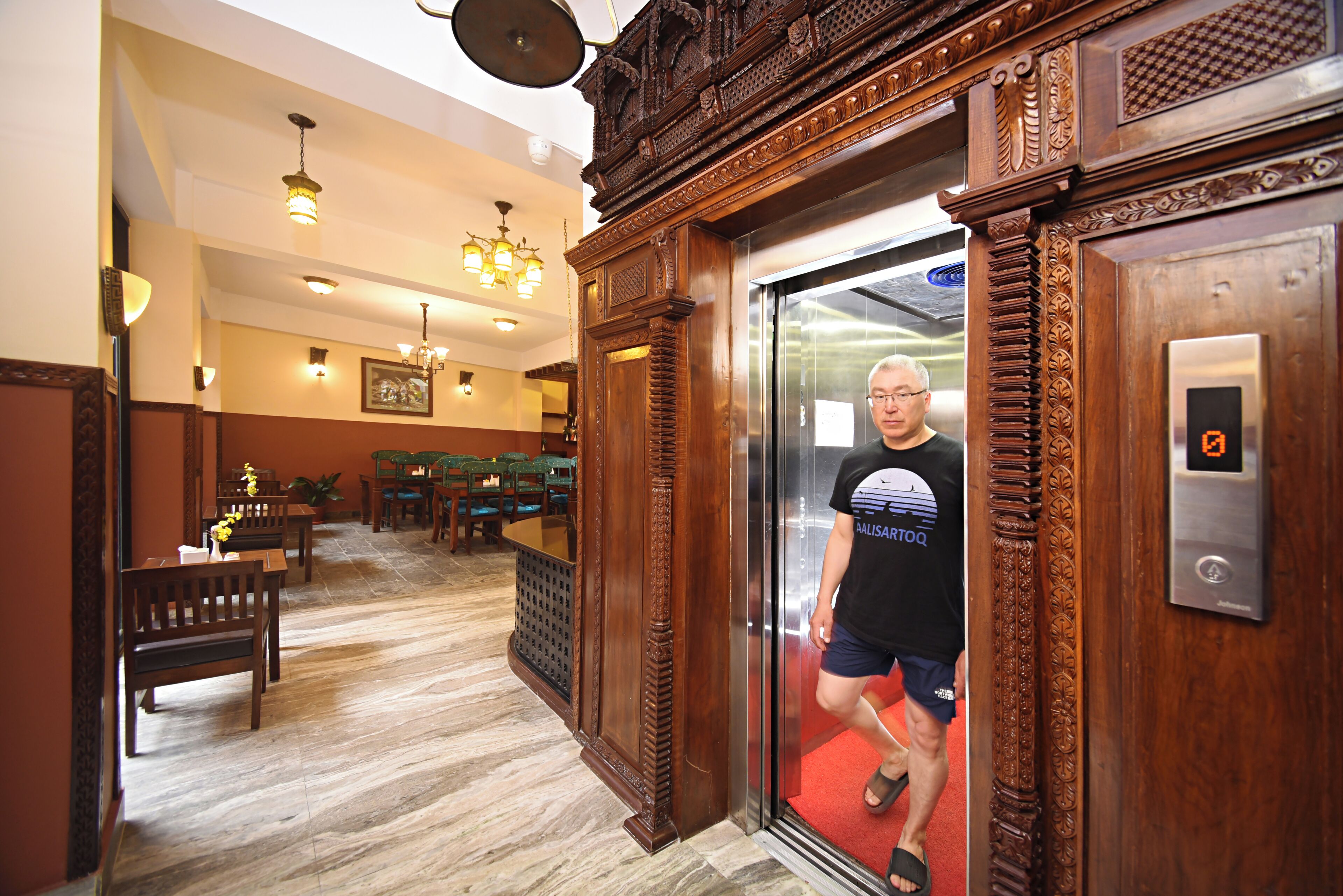 A hotel lobby with wooden decor, a reception desk, and a red carpet leading to an elevator.