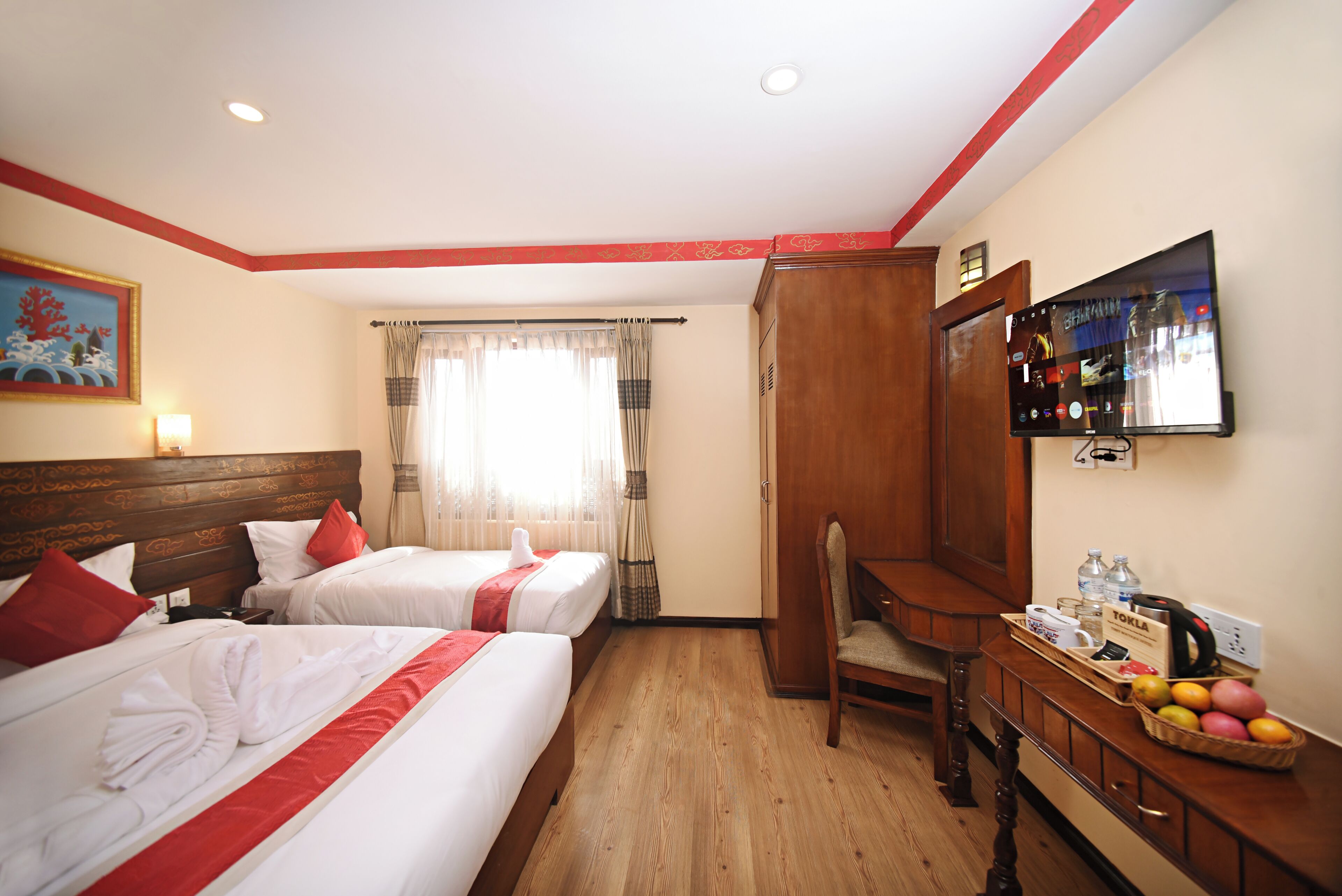 Quarto de hotel com duas camas, uma escrivaninha, uma cadeira, uma televisão e uma cesta de frutas.