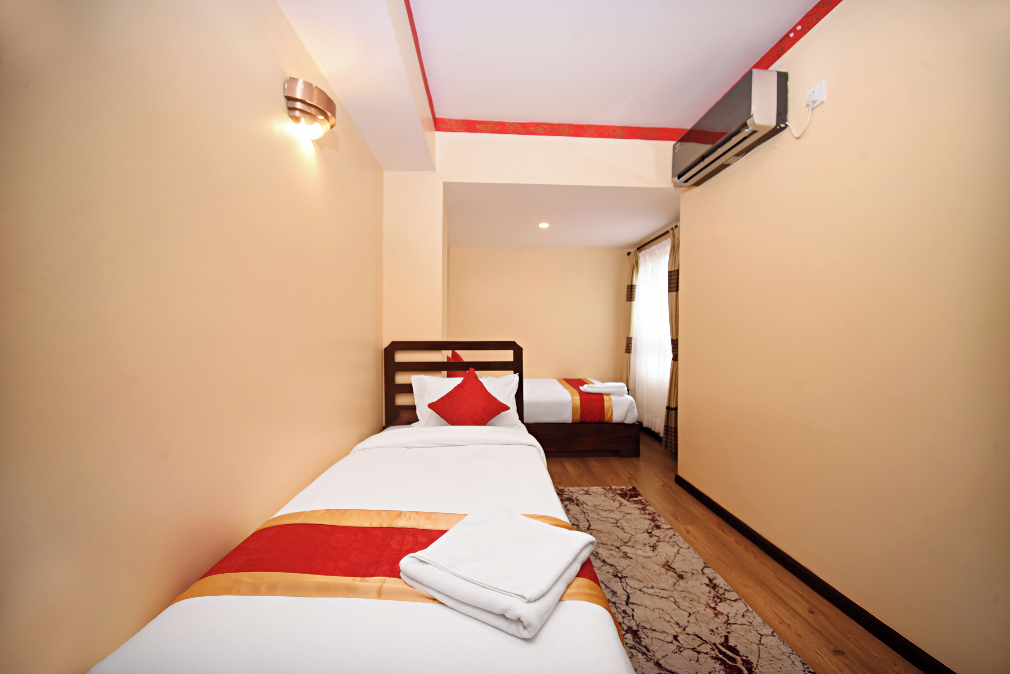 A hotel room with a single bed, a wooden headboard, a red and white striped pillow, and a neatly folded white towel.