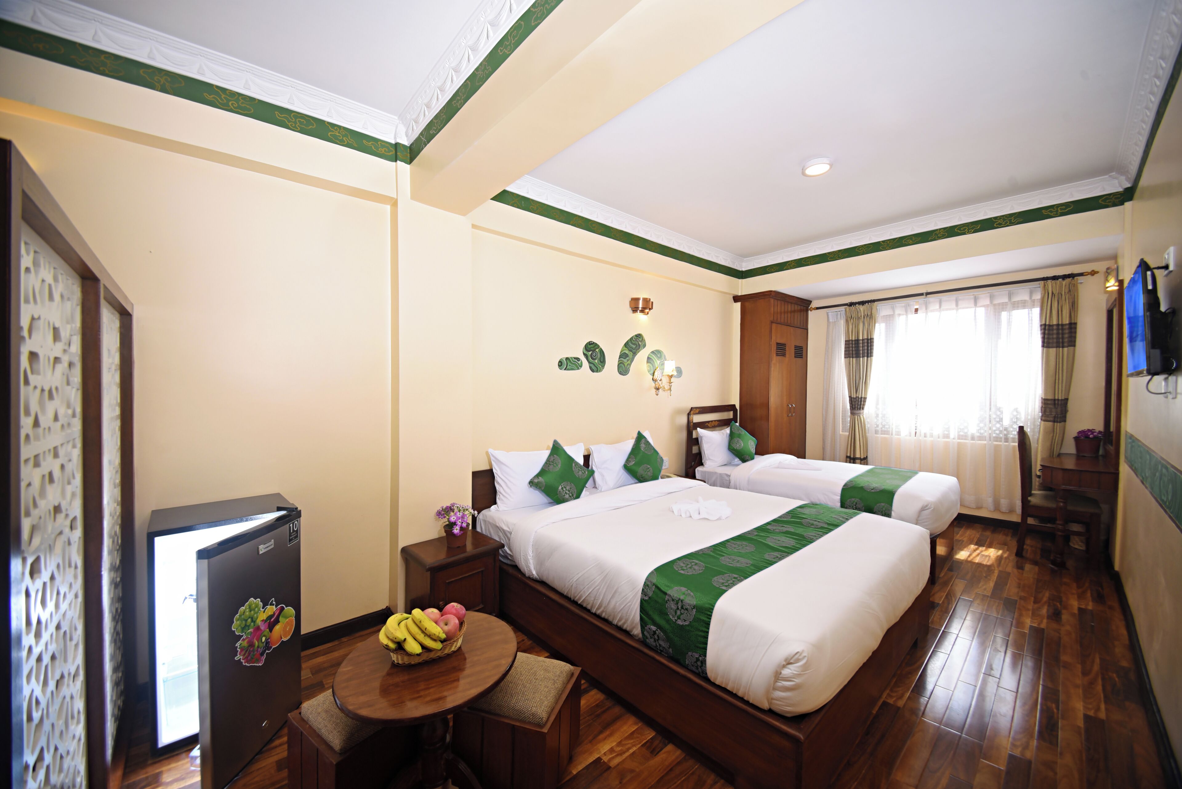 A hotel room with two beds, a refrigerator, a small table with fruit, and a wooden floor.