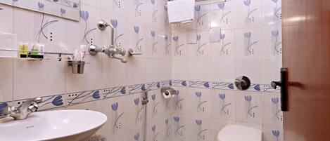 Un baño con lavamanos, inodoro y ducha. Hay toallas y artículos de aseo en la pared.