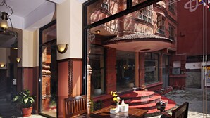 Zona pranzo con tavolo e sedie in legno, una pianta in vaso e vista su un edificio rosso con balconi.
