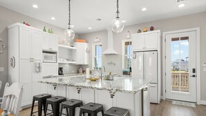 A modern kitchen with white cabinetry, a marble island, and black bar stools. - Parrot House-Ocean Side @ Pointe West-Close to walkover. 5BD/3Ba. Sleeps 15 (Galveston)