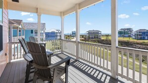 A covered porch with wooden chairs and a table, overlooking a beachfront community with houses and a clear sky. - Parrot House-Ocean Side @ Pointe West-Close to walkover. 5BD/3Ba. Sleeps 15 (Galveston)