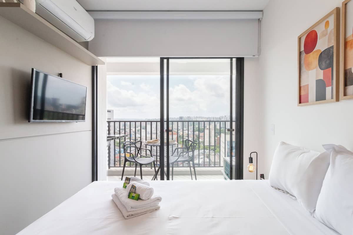 Habitación de hotel con cama, televisión, balcón con sillas y una mesa, y obras de arte en la pared.