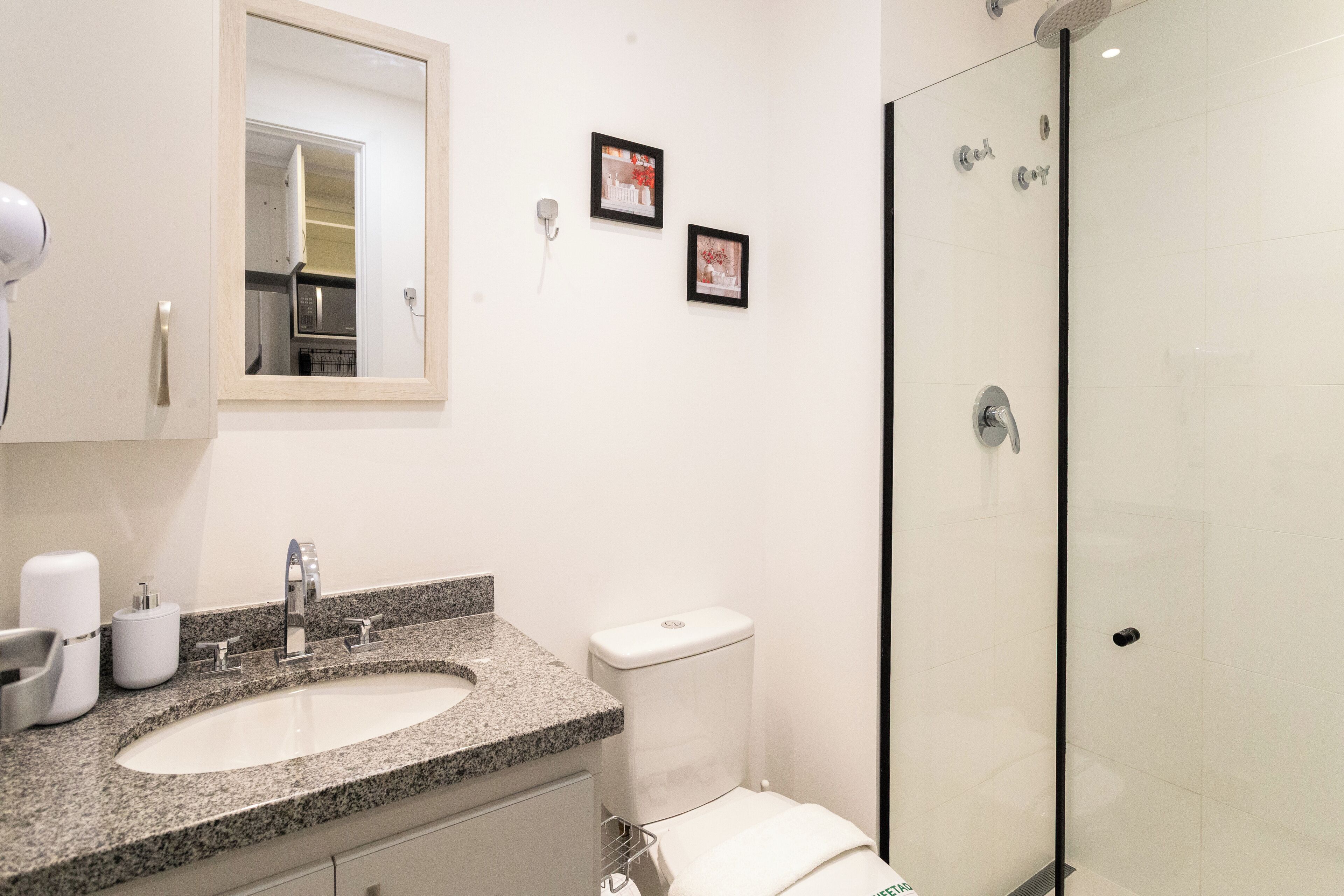 Un baño con lavamanos de encimera de granito, inodoro y ducha con mampara de vidrio.