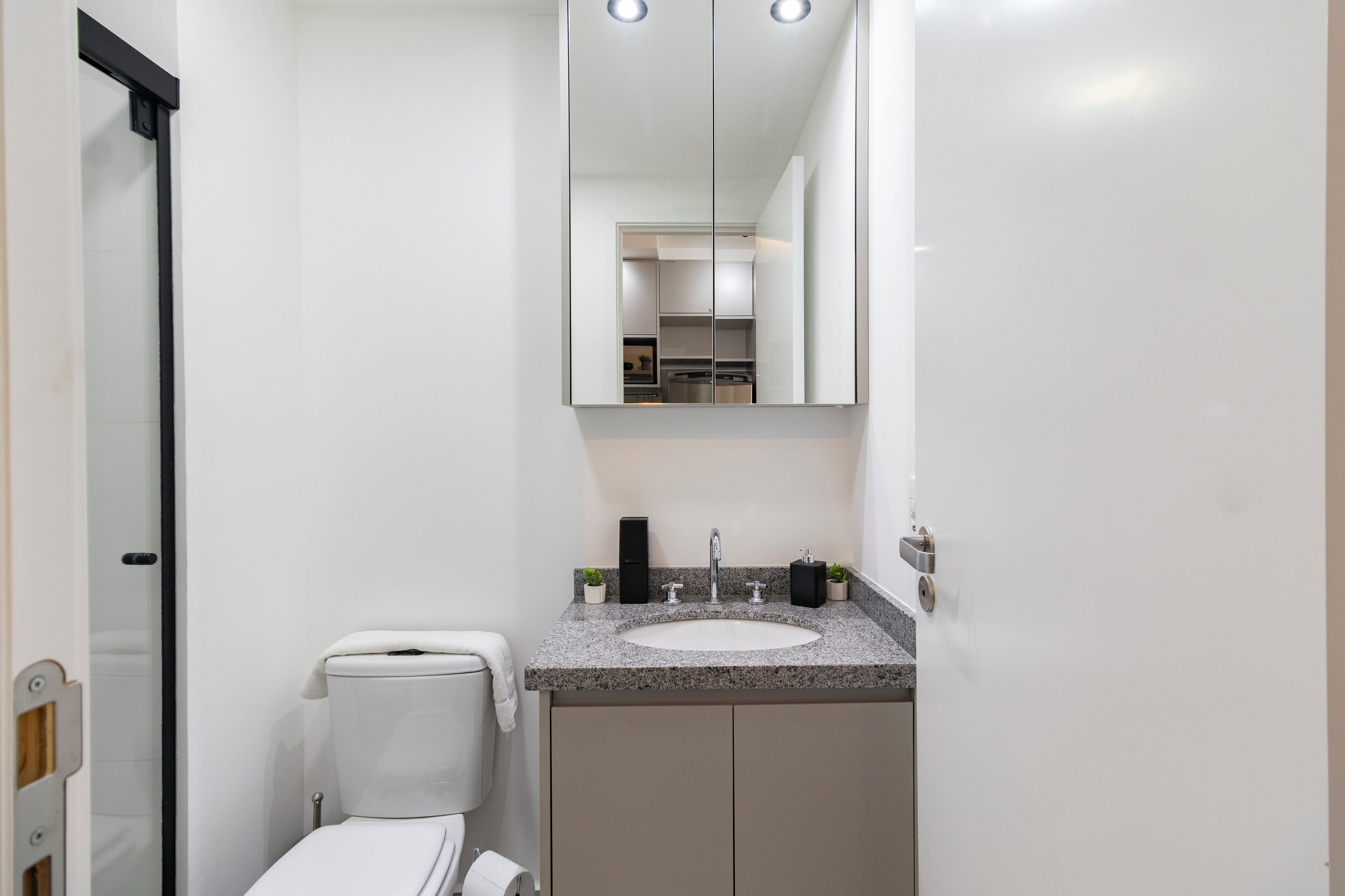 Une salle de bain moderne avec des toilettes blanches, un lavabo sur un plan de travail en granit et un grand miroir au-dessus du lavabo.