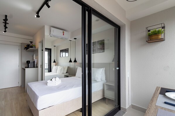 Une chambre d’hôtel moderne dotée d’un grand lit, d’une porte vitrée donnant sur un balcon, d’un petit bureau avec une chaise et d’une plante fixée au mur.