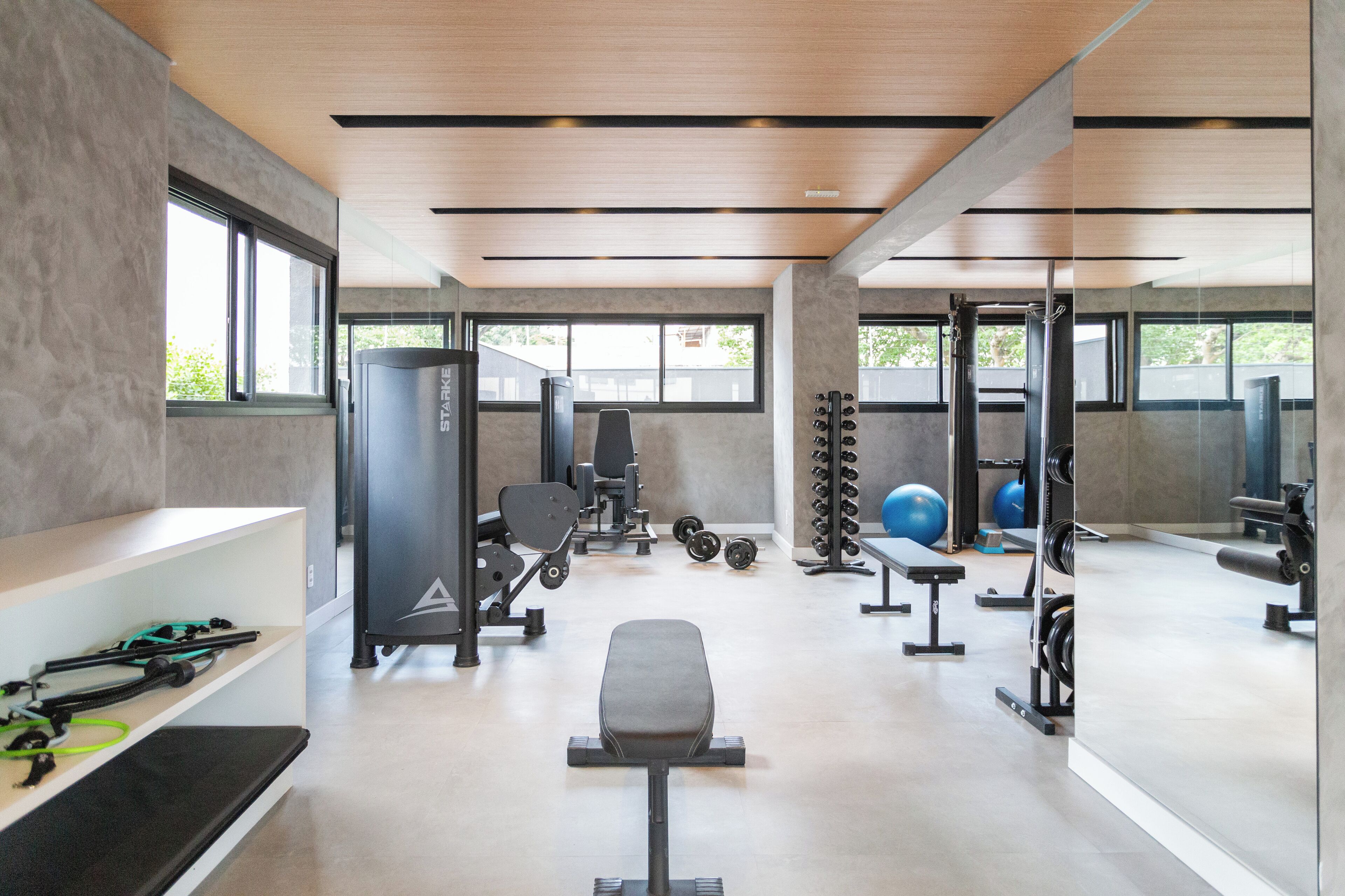 A modern gym with various exercise equipment, large windows, and a clean, minimalist design.