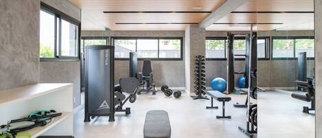 A modern gym with various exercise equipment, large windows, and a clean, minimalist design.