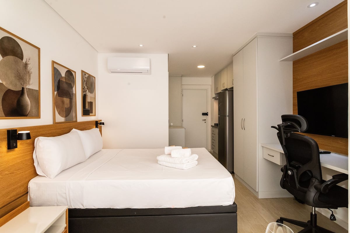 Una habitación de hotel moderna con una cama bien hecha, un escritorio con silla, un refrigerador y un televisor.
