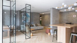 A modern interior with a sofa, glass partition, wooden flooring, and a bar area. - HUB Alto da Boa Vista (Sao Paulo)