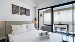 A modern hotel room with a large bed, white bedding, a cityscape artwork on the wall, a balcony with a table and chairs, and a hanging light fixture. - HUB Alto da Boa Vista (Sao Paulo)