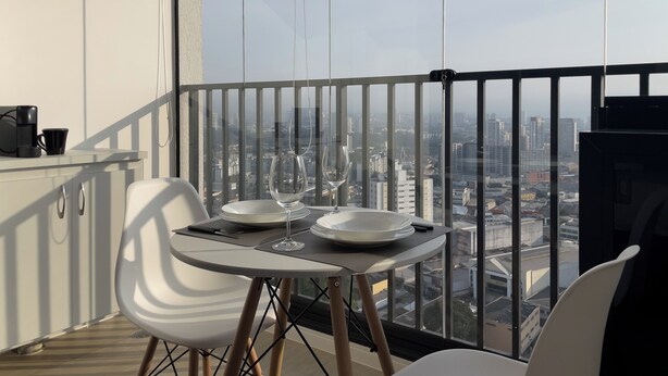 A balcony with a dining table set for two, a coffee maker, and a view of the cityscape. - HUB Alto da Boa Vista (Sao Paulo)
