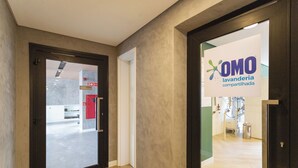 A hallway with a sign for 'OMO lavanderia compartilhada' and a door leading to a room with a wooden floor. - HUB Alto da Boa Vista (Sao Paulo)