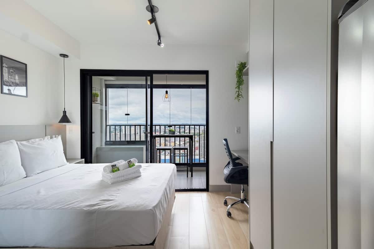 Una habitación de hotel moderna con una cama grande, un escritorio, una silla y un balcón con vistas.