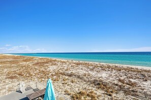A beach with a wooden deck and a turquoise umbrella.