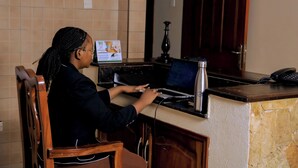 A person seated at a desk with a laptop, a telephone, and a vase. - Entebbe Coffee Lodge (Entebbe)