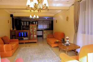 A living room with orange sofas, a wooden coffee table, and a TV. - Entebbe Coffee Lodge (Entebbe)