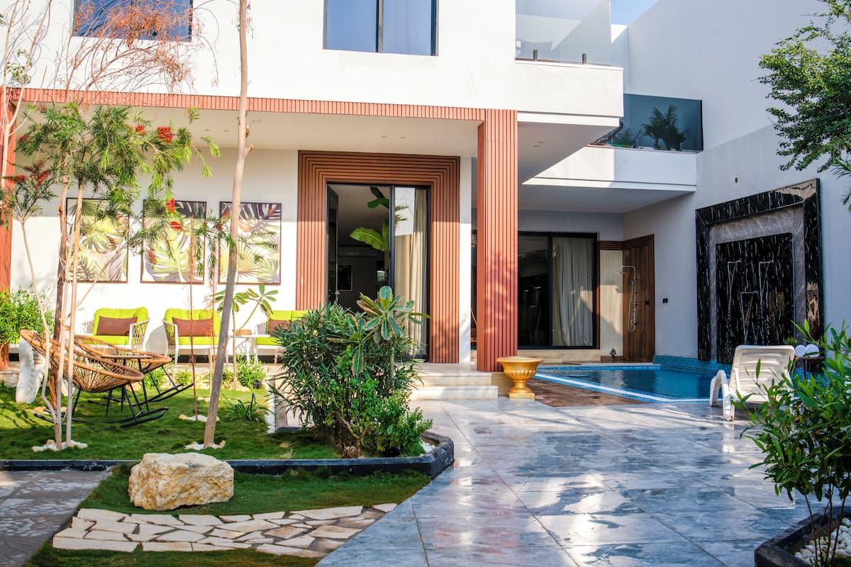 A modern outdoor pool area with a stone pathway, lounge chairs, and a small garden with plants and a rock.