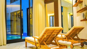 Una habitación con puerta de vidrio que da a una piscina, dos sillones de madera y un espejo grande en la pared.