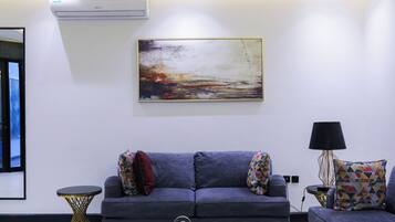A modern living room with a grey sofa, a colorful abstract painting, and a small side table with a lamp.