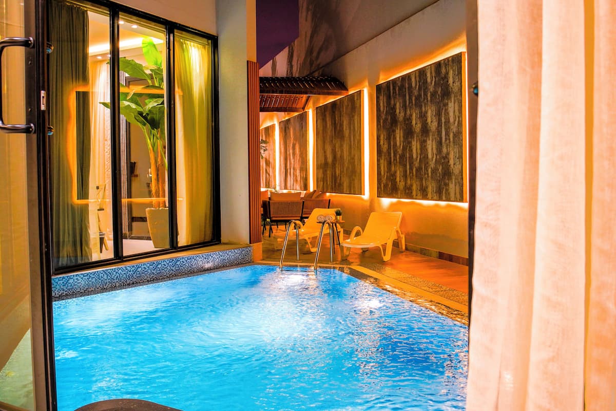 An indoor swimming pool with clear water, surrounded by lounge chairs and a glass door leading to a room with a plant and a table.