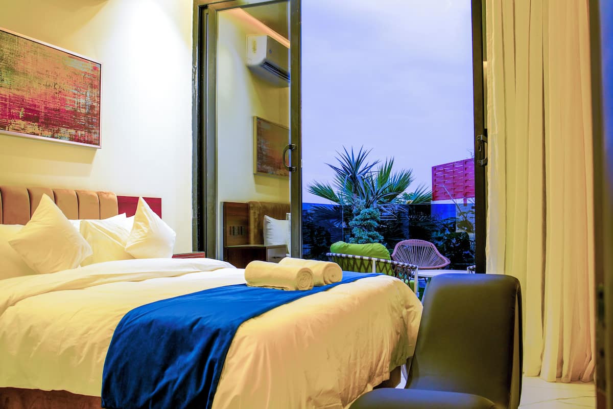 A hotel room with a bed, a chair, a desk, and a view of the outside.