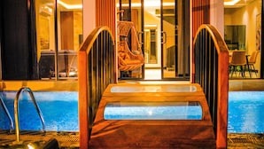 Zona de piscina amb un banyera d'hidromassatge, una cadira de relax i una zona de menjador visibles a través de les portes de vidre.
