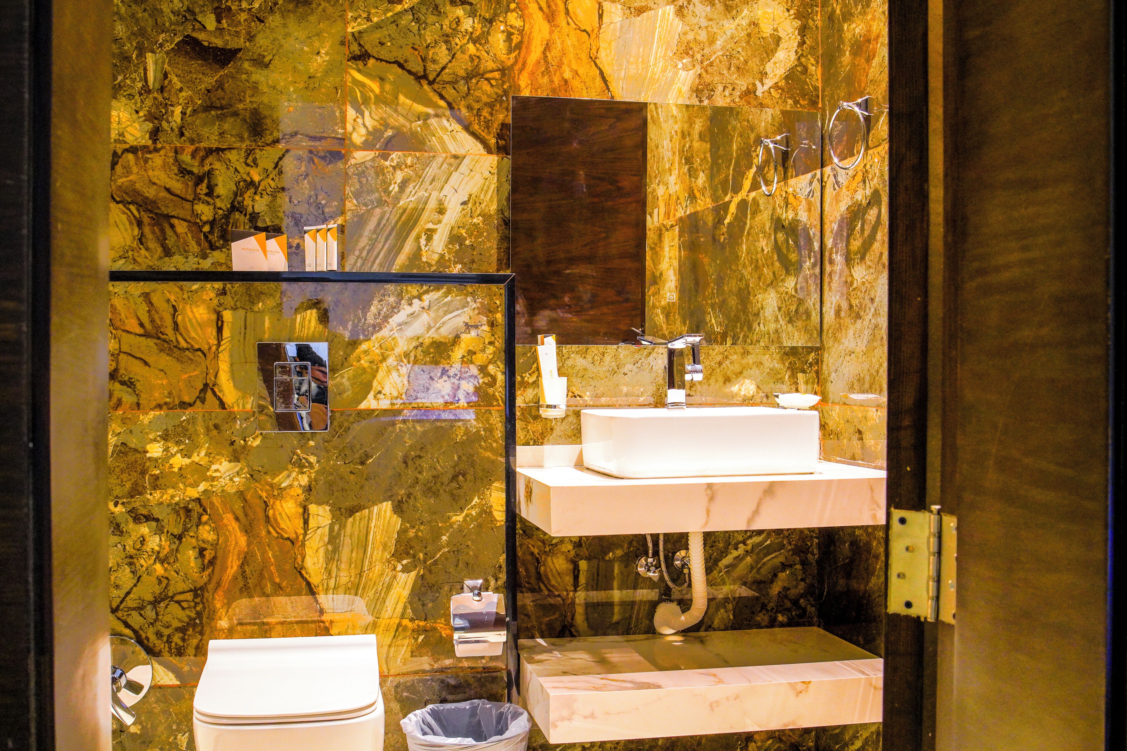 A bathroom with a marble wall, a white sink, and a toilet.