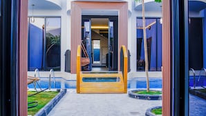 Entrada d'un hotel modern amb zona de piscina, una escala de fusta i una cadira relax.