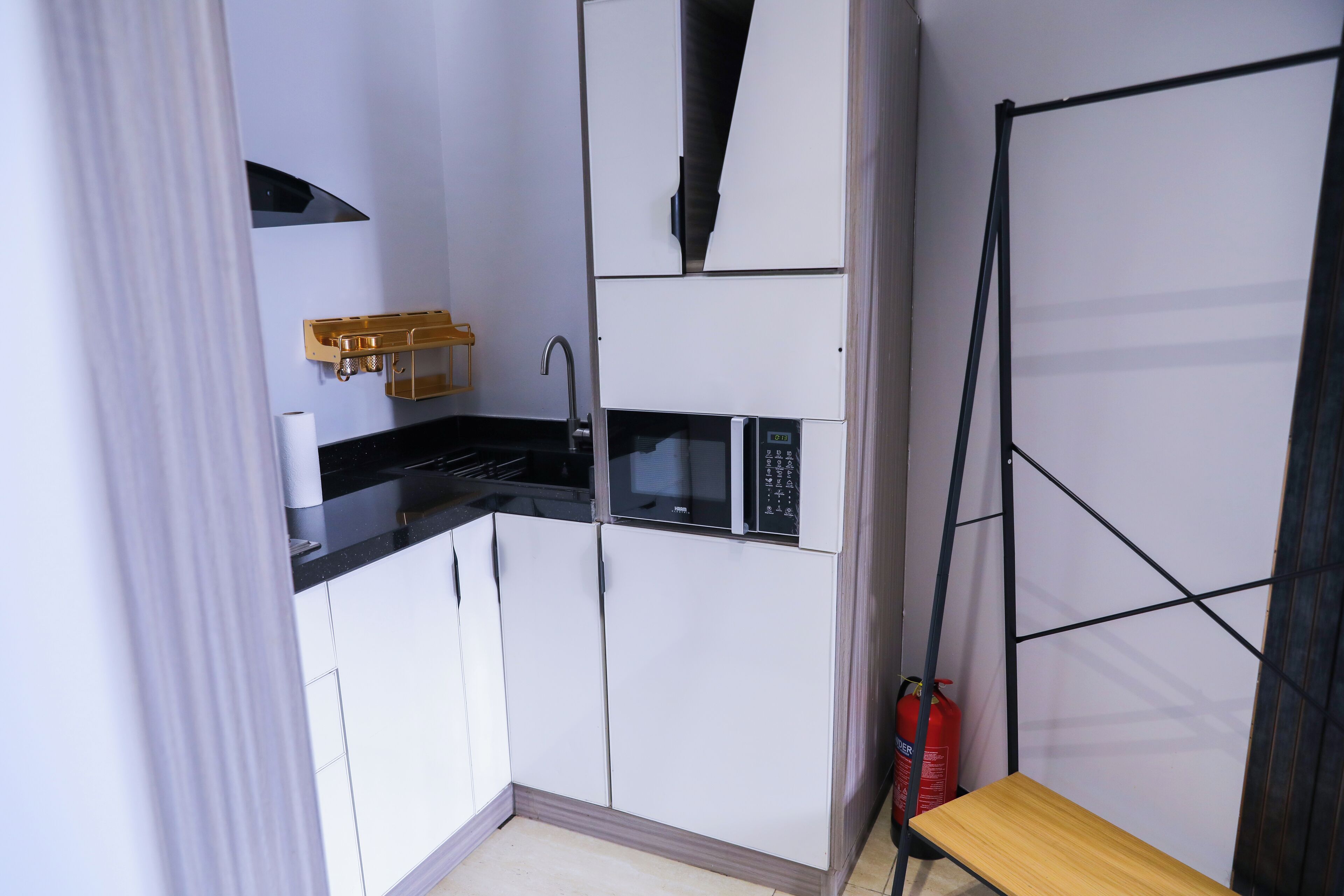 A compact kitchen with white cabinets, a black countertop, a microwave, and a fire extinguisher.