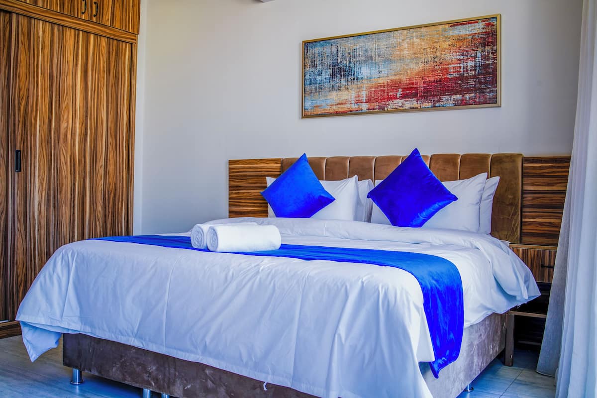 A neatly made bed with white and blue bedding, a wooden headboard, and a large abstract painting on the wall.