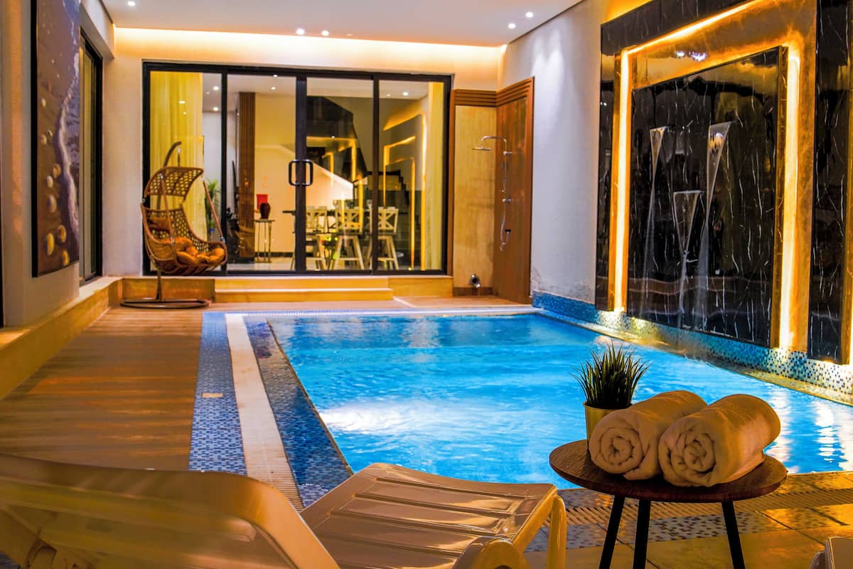 An indoor swimming pool with a glass wall, a chair, and towels on a table.