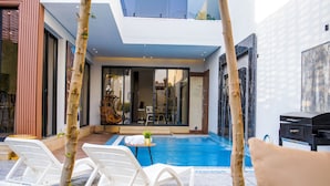 Zona de piscina exterior moderna amb gandules, una taula petita amb una planta i vista cap a l'interior a través de portes de vidre.