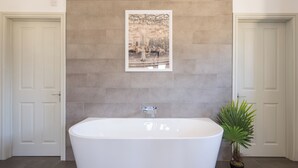 A bathroom with a freestanding bathtub, a framed picture on the wall, and a potted plant.