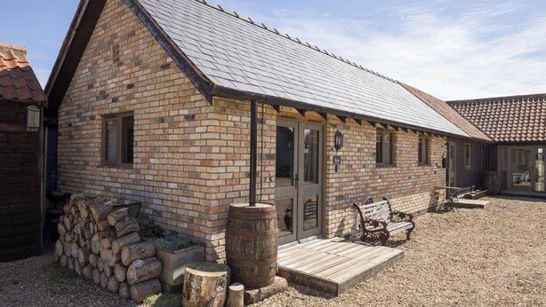 A brick building with a sloped roof, a wooden deck, and a stack of firewood.