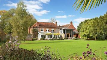 Traditional home with a spacious lawn and a conservatory offering an enclosed outdoor space surrounded by lush greenery.